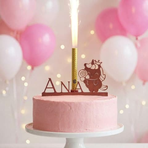 Personalised unicorn cake topper with a child's name and a lit ice fountain on a pink birthday cake